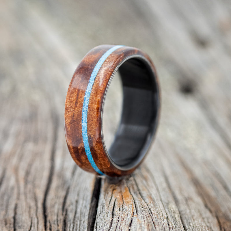 Shown here is "Remmy", a custom, handcrafted men's wedding ring featuring a redwood overlay and an offset turquoise inlay, shown here on a fire-treated black zirconium band, upright facing left. Additional inlay options are available upon request.