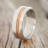 Shown here is "Vertigo", a custom, handcrafted men's wedding ring featuring an olive wood inlay with a hammered finish, upright facing left. Additional inlay options are available upon request.