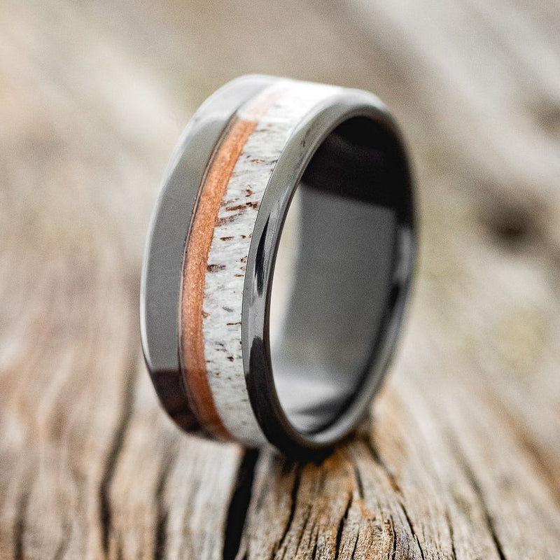 Shown here is "Tanner", a custom, handcrafted men's wedding ring featuring an antler and powdered copper inlay, shown here on a fire-treated black zirconium band, upright facing left. Additional inlay options are available upon request.
