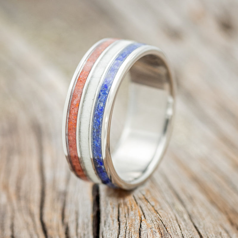 Shown here is "Rio", a custom, handcrafted men's wedding ring featuring 3 channels with red opal, antler, and lapis lazuli inlays, upright facing left.