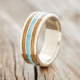 Shown here is "Rio", a custom, handcrafted men's wedding ring featuring 3 channels with a whiskey barrel and turquoise inlays on a 14K gold band, upright facing left. Additional inlay options are available upon request.