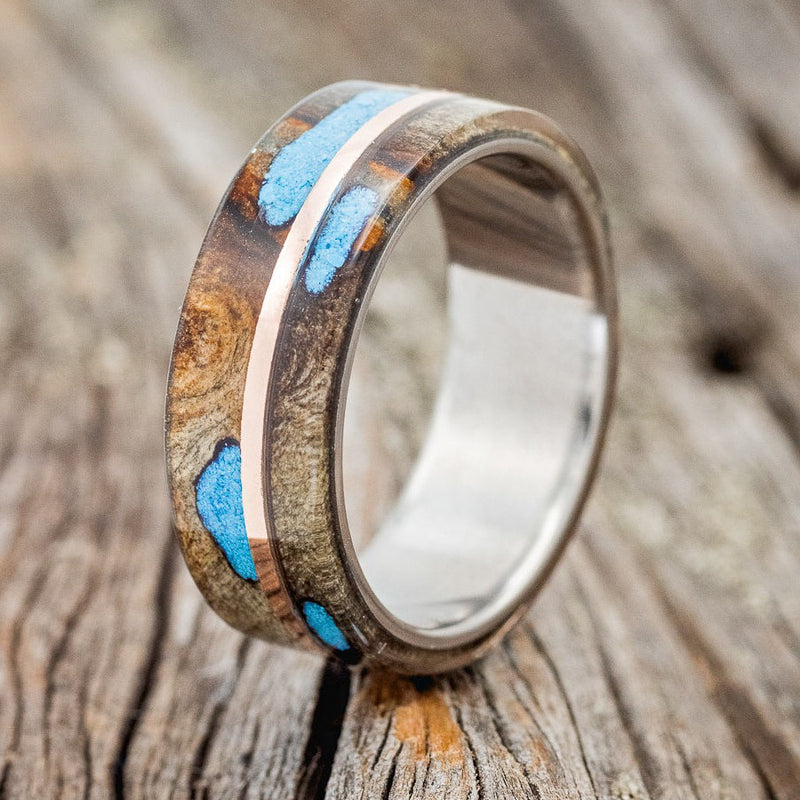 Shown here is "Golden", a custom, handcrafted men's wedding ring featuring a buckeye burl overlay, with turquoise set into burls, divided by a 14K rose gold inlay, upright facing left. Additional inlay options are available upon request.