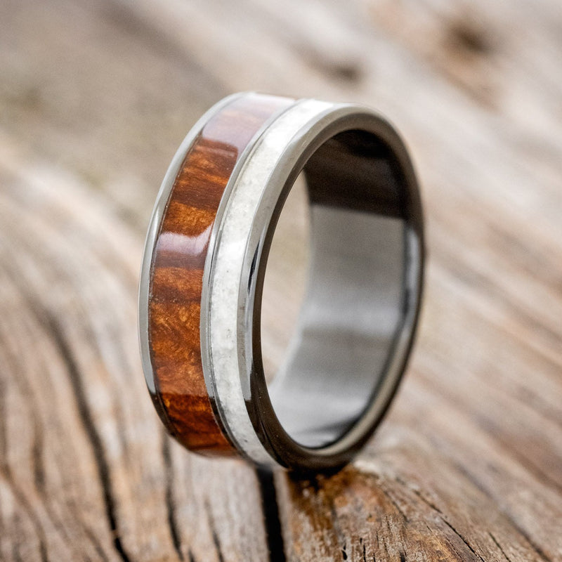 Shown here is "Raptor", a custom, handcrafted men's wedding ring featuring granite and redwood inlays on a fire-treated black zirconium band, upright facing left. Additional inlay options are available upon request.