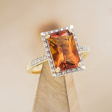 Shown here is "Sienna", an emerald cut madeira citrine women's engagement ring with diamond halo and diamond accents, on stand facing slightly right. Many other center stone options are available upon request.