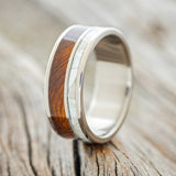 Shown here is "Raptor", a custom, handcrafted men's wedding ring featuring ironwood and mother of pearl inlays on a titanium band, upright facing left. Additional inlay options are available upon request.