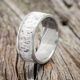 Shown here is "Rainier", a custom, handcrafted men's wedding ring featuring an antler inlay, shown here on an etched Damascus steel band, upright facing left. Additional inlay options are available upon request.