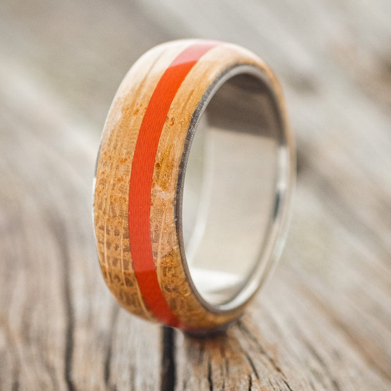 Shown here is "Remmy", a custom, handcrafted men's wedding ring featuring a whiskey barrel oak overlay and a red G10 inlay, shown here on a titanium band, upright facing left. Additional inlay options are available upon request.
