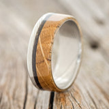 Shown here is "Ezra", a custom, handcrafted men's wedding ring featuring a whiskey barrel oak overlay and a charred whiskey barrel inlay, upright facing left. Additional inlay options are available upon request.