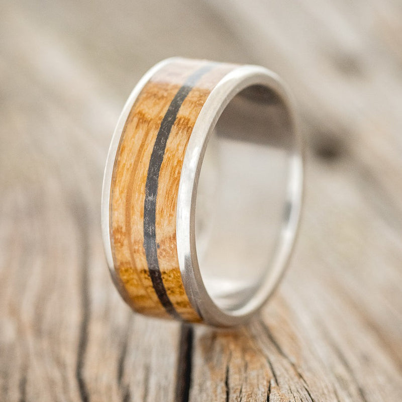 Shown here is "Rainier", a custom, handcrafted men's wedding ring featuring a whiskey barrel and charred whiskey barrel inlay on a titanium band, upright facing left. Additional inlay options are available upon request.
