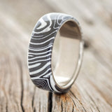 Shown here is "Haven", a custom, handcrafted men's wedding ring featuring a white and black G10 wave overlay, upright facing left. Additional inlay options are available upon request.