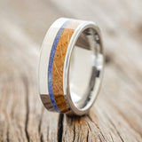 Shown here is "Tanner", a custom, handcrafted men's wedding ring featuring a whiskey barrel and a lapis lazuli inlays on a tungsten band, upright facing left. Additional inlay options are available upon request.
