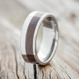 Shown here is "Tanner", a custom, handcrafted men's wedding ring featuring a walnut wood inlay, upright facing left. Additional inlay options are available upon request.