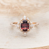 Shown here is "North Star", an oval garnet women's engagement ring with a diamond halo and accents, front facing. Many other center stone options are available upon request.