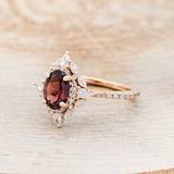 Shown here is "North Star", an oval garnet women's engagement ring with a diamond halo and accents, facing left. Many other center stone options are available upon request.