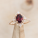 Shown here is "North Star", an oval garnet women's engagement ring with a diamond halo and accents, on stand front facing. Many other center stone options are available upon request.