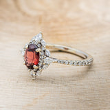 Shown here is "North Star", an oval garnet women's engagement ring with a diamond halo and accents, facing left. Many other center stone options are available upon request.