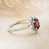 Shown here is "North Star", an oval garnet women's engagement ring with a diamond halo and accents, facing right. Many other center stone options are available upon request.