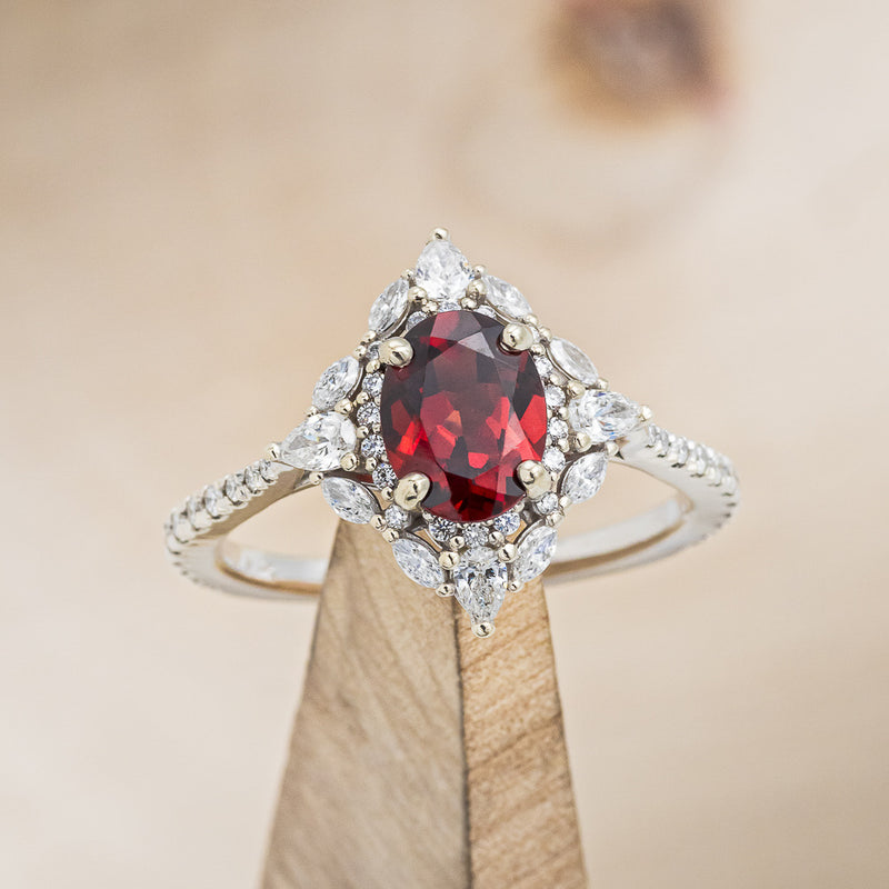 Shown here is "North Star", an oval garnet women's engagement ring with a diamond halo and accents, on stand front facing. Many other center stone options are available upon request.
