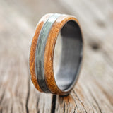 Shown here is "Glen", a custom, handcrafted men's wedding ring featuring whiskey barrel oak overlays and a fishing line inlay on a fire-treated black zirconium band, upright facing left. Additional inlay options are available upon request.