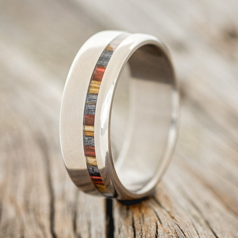Shown here is "Vertigo", a handcrafted men's wedding ring featuring an offset inlay with red, grey and brown birch wood, upright facing left. Additional inlay options are available upon request.