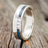 Shown here is "Vertigo", a custom, handcrafted men's wedding ring featuring a 14K gold wedding band featuring 3 offset diamonds and a patina copper inlay, upright facing left. Additional inlay options are available upon request.