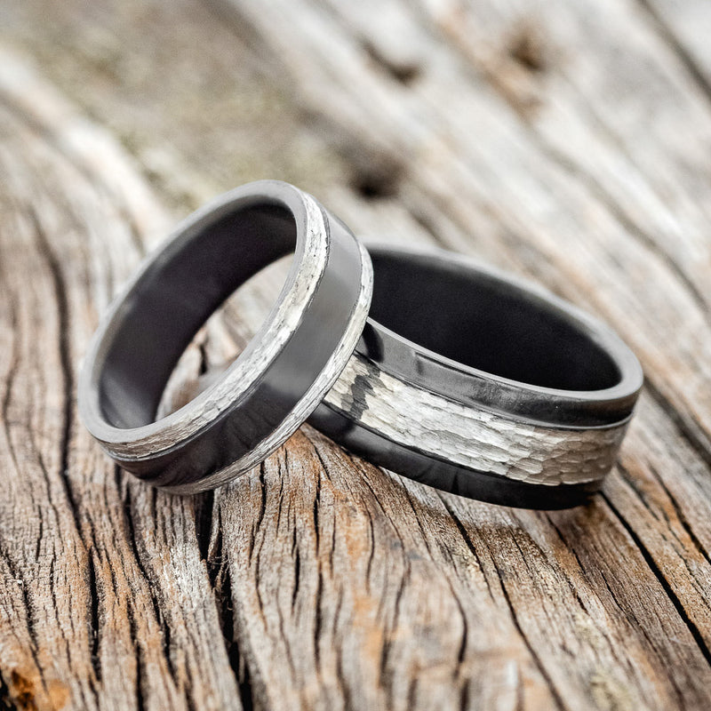 Shown here is a matching wedding band set featuring 2 "Sedona" black zirconium bands hammered after its been fire-treated, laying together. One ring has the hammered finish on the raised center and the other ring has the hammered finish on the edges of the ring. You will need to note in the Custom Requests what size you want the hammered-edged ring to be, and what size you want the hammered center ring to be.
