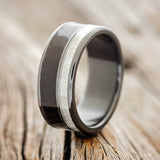 Shown here is "Raptor", a custom, handcrafted men's wedding ring featuring African black wood & naturally shed elk antler inlays on a fire-treated black zirconium band, upright facing left. Additional inlay options are available upon request.