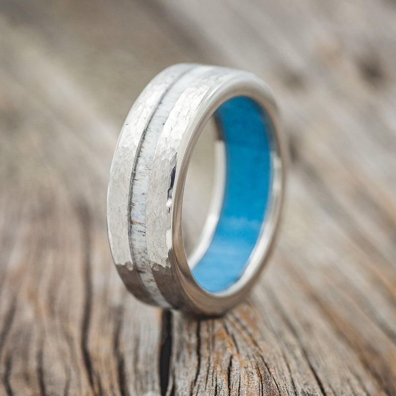 Shown here is "Vertigo", a custom, handcrafted men's wedding ring featuring an offset antler inlay with a turquoise lining and hammered band, upright facing left. 