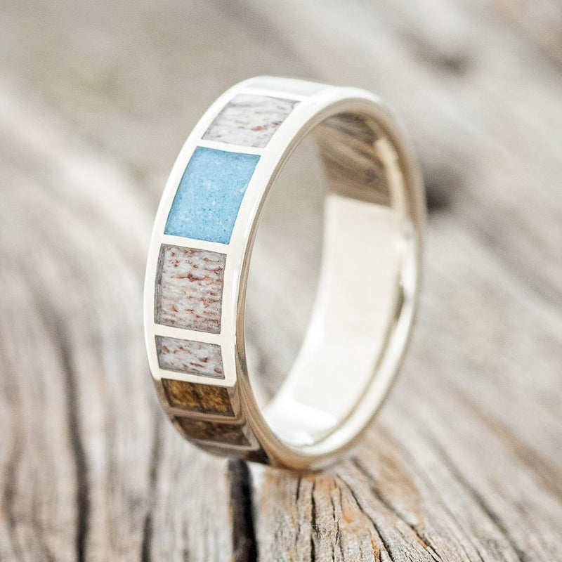 Shown here is a custom, handcrafted men's wedding ring featuring antler, turquoise, and buckeye burl wood inlays, upright facing left. Additional inlay options are available upon request.