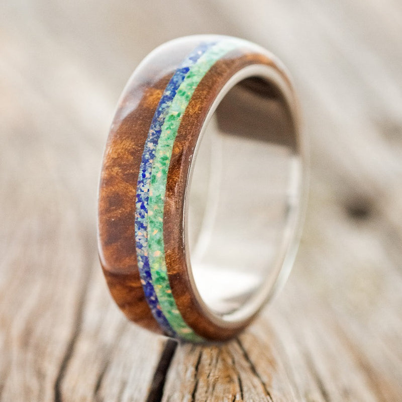 Shown here is "Remmy", a custom, handcrafted men's wedding ring featuring a redwood overlay with blue opal and malachite inlay on a titanium band, upright facing left. Both the blue opal and the malachite are mixed with opal. Additional inlay options are available upon request.