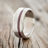Shown here is "Vertigo", a custom, handcrafted men's wedding ring featuring an offset purpleheart wood inlay with a hammered finish, upright facing left.