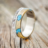 Shown here is "Golden", a custom, handcrafted men's wedding ring featuring one overlay with buckeye burl and turquoise inlays and a second overlay with naturally shed antler, upright facing left.