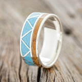 Shown here is "Cadence", a custom, handcrafted men's wedding ring featuring a whiskey barrel inlay & turquoise triangle inlays, upright facing left. Additional inlay options are available upon request.