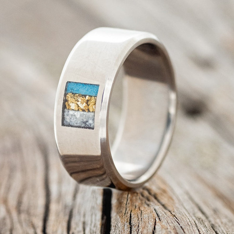 Shown here is a custom, handcrafted men's wedding ring featuring a square inlay with turquoise, gold nuggets and diamond dust, upright facing left. Additional inlay options are available upon request.