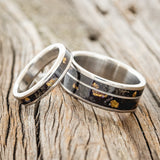Shown here is a matching wedding band set featuring "Eterna" & "Raptor", laying together. "Eterna" is a wide women's stacking band featuring a buckeye burl and gold nugget inlays. "Raptor" is a handcrafted wide wedding band featuring 2 channels with buckeye burl wood and gold nugget inlays. Additional inlay options are available upon request.