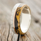 Shown here is "Golden", a custom, handcrafted men's wedding ring featuring one overlay with buckeye burl and gold nugget inlays and another overlay with antler, upright facing left. These two overlays are divided by a 14K rose gold inlay. Additional inlay options are available upon request.