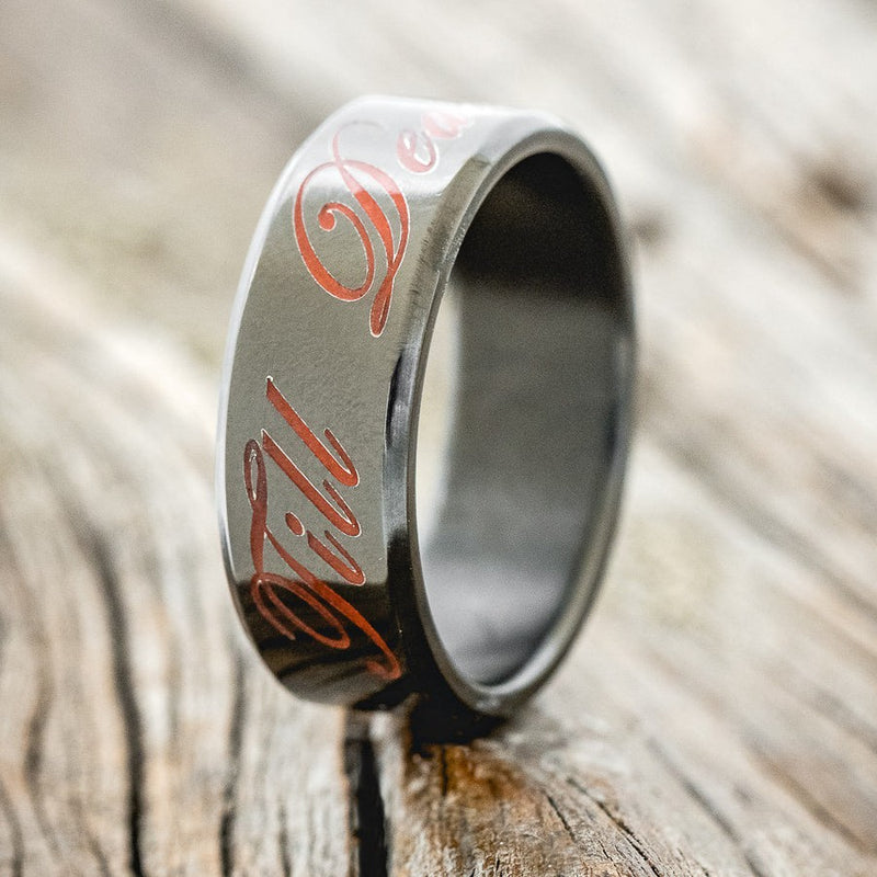 Shown here is "Till Death", a custom, handcrafted wedding band with a glow-in-the-dark engraving, upright facing left. It can be customized to feature just about any engraved design you can dream up.