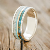 Shown here is "Element", a custom, handcrafted men's wedding ring featuring patina copper, a thin 14K yellow gold inlay, turquoise, and antler inlays, upright facing left. Additional inlay options are available upon request.
