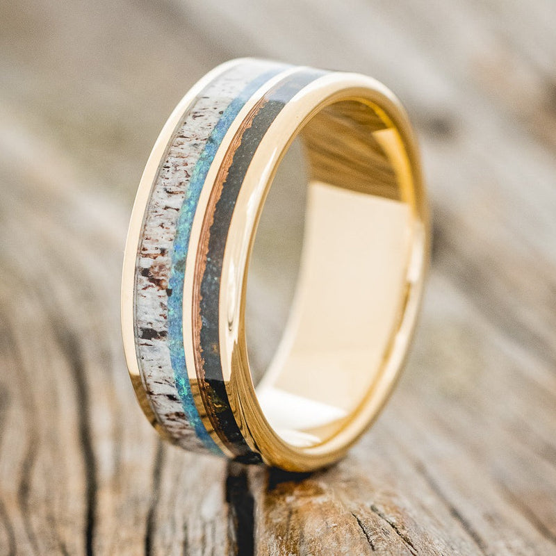 Shown here is "Element",  a custom, handcrafted men's wedding ring featuring patina copper, blue opal, and antler inlays on a 14K gold band, upright facing left. Additional inlay options are available upon request.