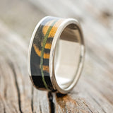 Shown here is "Rainier", a custom, handcrafted men's wedding ring featuring black and white ebony with an offset moss inlay on a titanium band, shown facing right. Additional inlay options are available upon request.