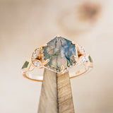 Shown here is "Lucy in the Sky", a hexagon moss agate women's engagement ring with a diamond halo and moss inlays, on stand front facing. Many other center stone options are available upon request.