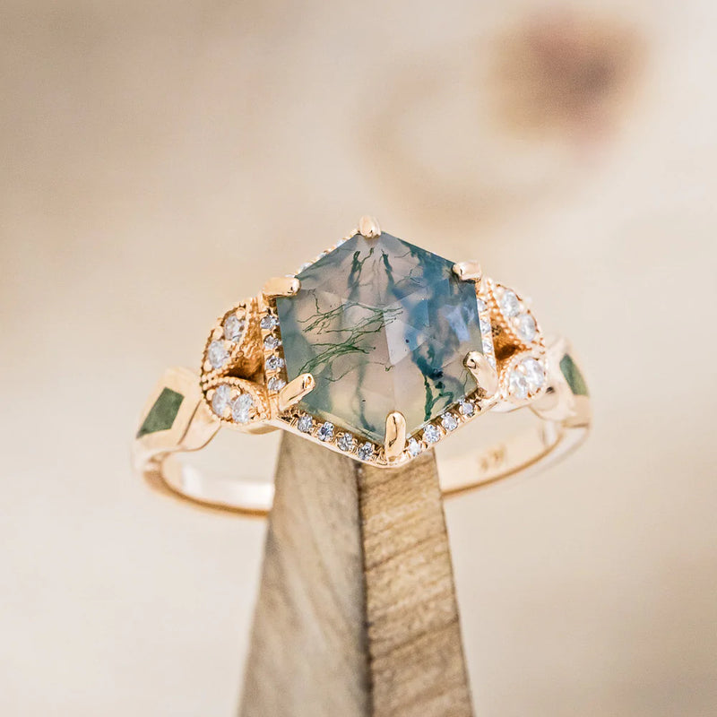 Shown here is "Lucy in the Sky", a hexagon moss agate women's engagement ring with a diamond halo and moss inlays, on stand front facing. Many other center stone options are available upon request.