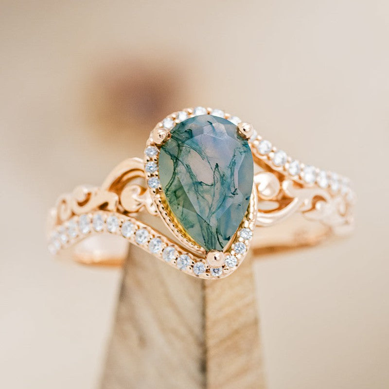 Shown here is "Scarlet", a pear-shaped moss agate women's engagement ring with diamond accents, on stand front facing. Many other center stone options are available upon request.