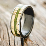 Shown here is "Rainier", a handcrafted men's wedding ring featuring moss and spalted maple wood inlays on a fire-treated black zirconium band, upright facing left. Additional inlay options are available upon request.
