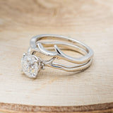 Shown here is "Artemis", a moissanite women's engagement ring with an antler/branch style stacking band, facing left. Many other center stone options are available upon request.
