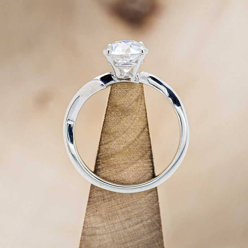 Shown here is "Artemis", a moissanite women's engagement ring with an antler/branch style band, side view on stand. Many other center stone options are available upon request.