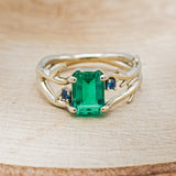 Shown here is "Artemis", an antler/branch-style lab-created emerald women's engagement ring with sapphire accents, front facing. Many other center stone options are available upon request.