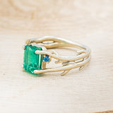Shown here is "Artemis", an antler/branch-style lab-created emerald women's engagement ring with sapphire accents, facing left. Many other center stone options are available upon request.
