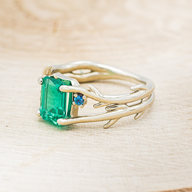 Shown here is "Artemis", an antler/branch-style lab-created emerald women's engagement ring with sapphire accents, facing left. Many other center stone options are available upon request.