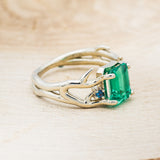 Shown here is "Artemis", an antler/branch-style lab-created emerald women's engagement ring with sapphire accents, facing right. Many other center stone options are available upon request.